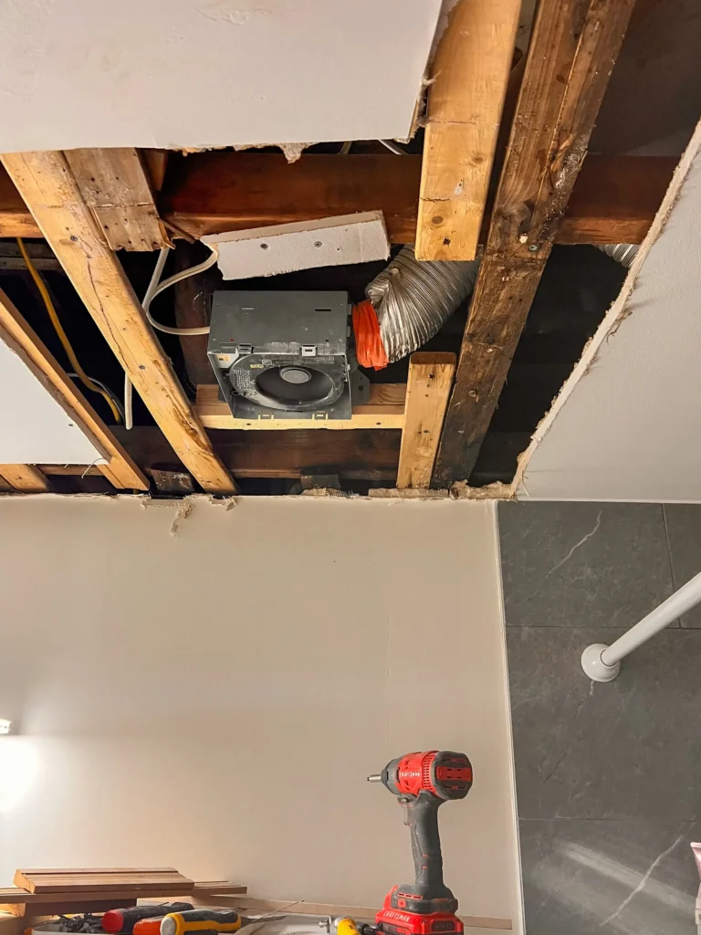 Open ceiling showing framing, ductwork, and a ventilation fan during repair