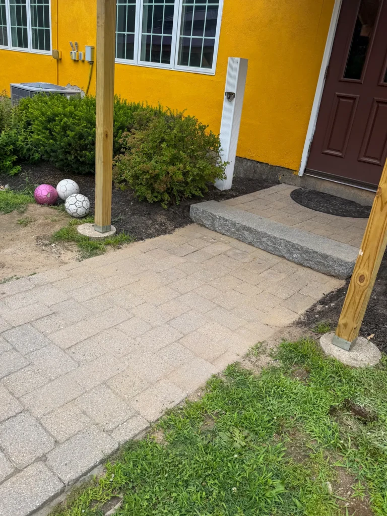 Paver walkway and granite entry step beside a yellow building